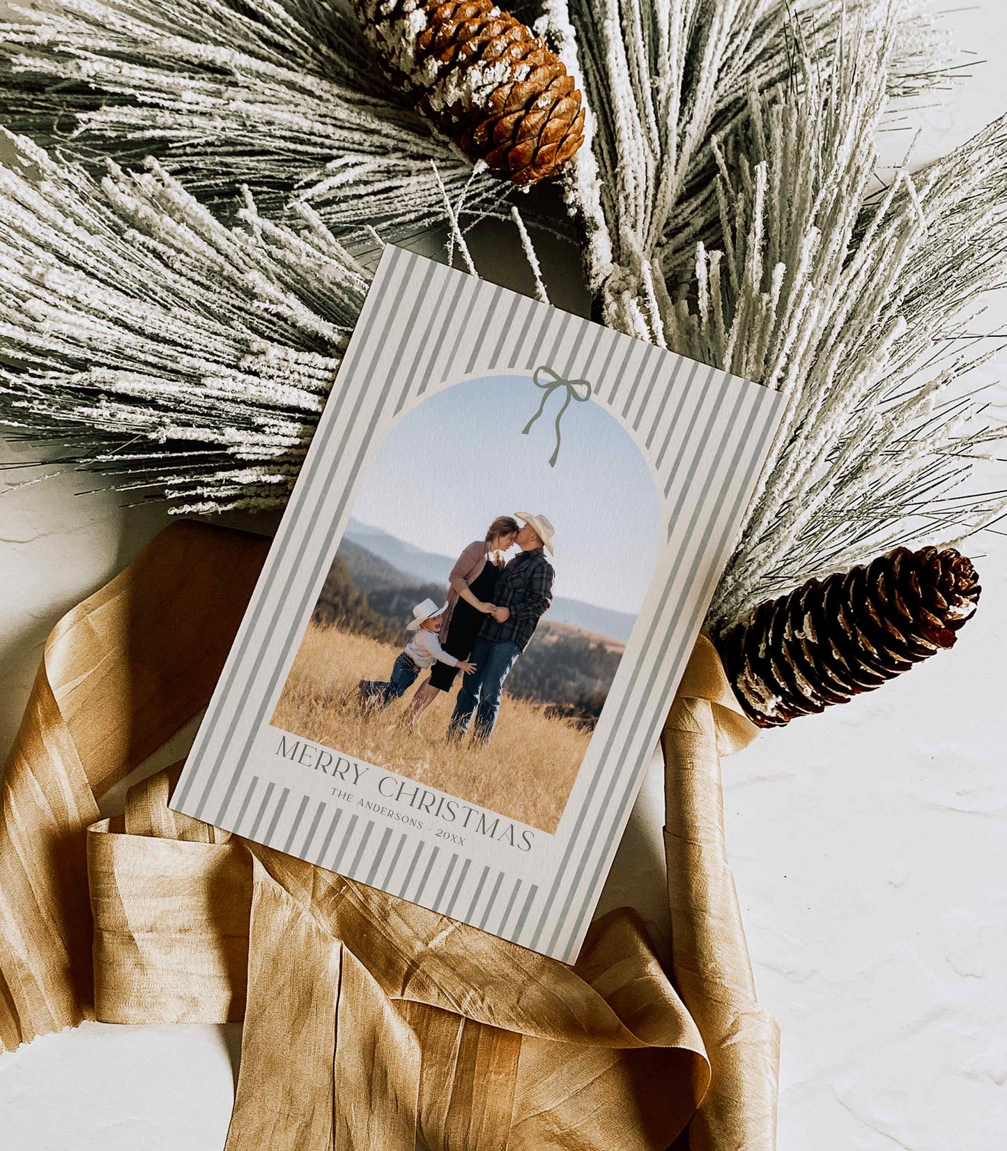 Christmas card with a photo of a couple and child, surrounded by decorative elements like pine cones and straw.