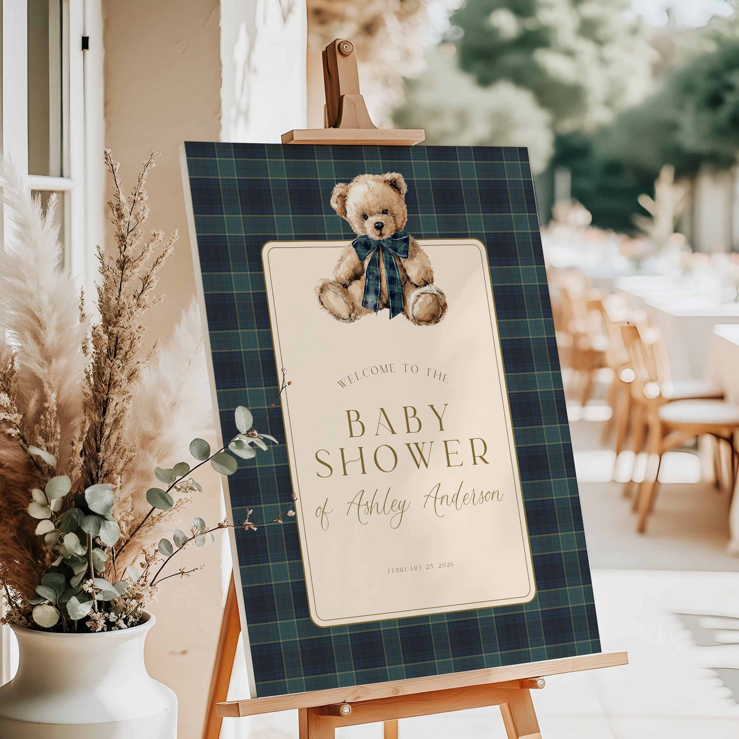 Baby shower welcome sign with teddy bear on a plaid background, placed on an easel.