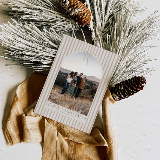 Christmas card with a photo of a family on a snowy landscape, surrounded by decorative branches and pinecones.