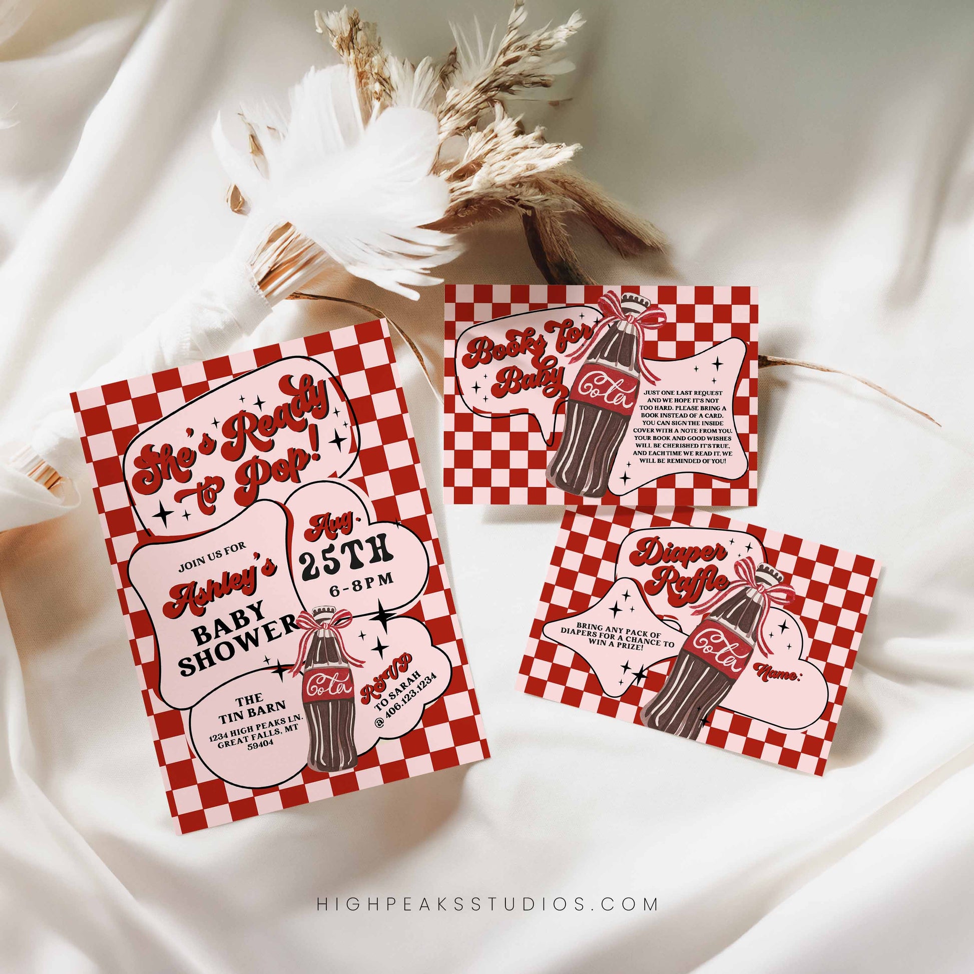 Red and white checkered baby shower invitations with Cola theme on a white fabric background.