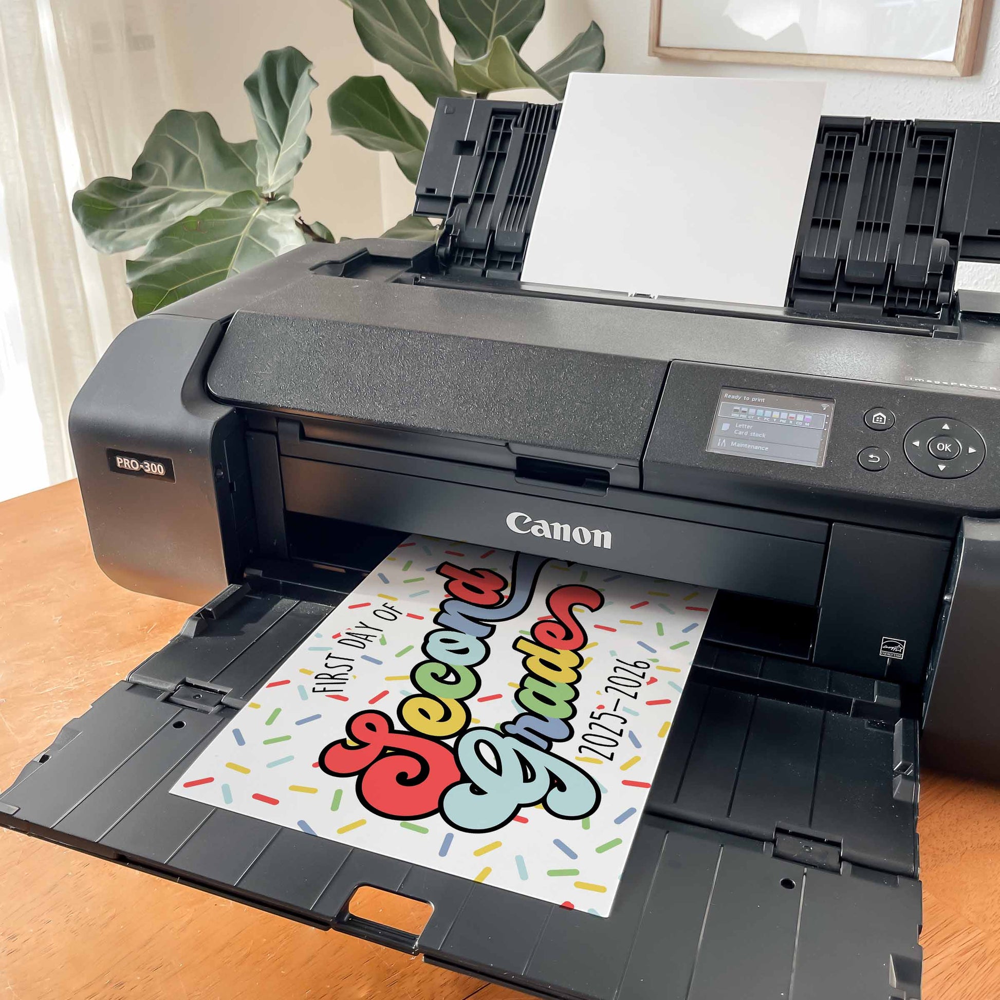 Canon printer printing a colorful back to second grade school sig on a wooden table with plants in the background By High Peaks Studios LLC
