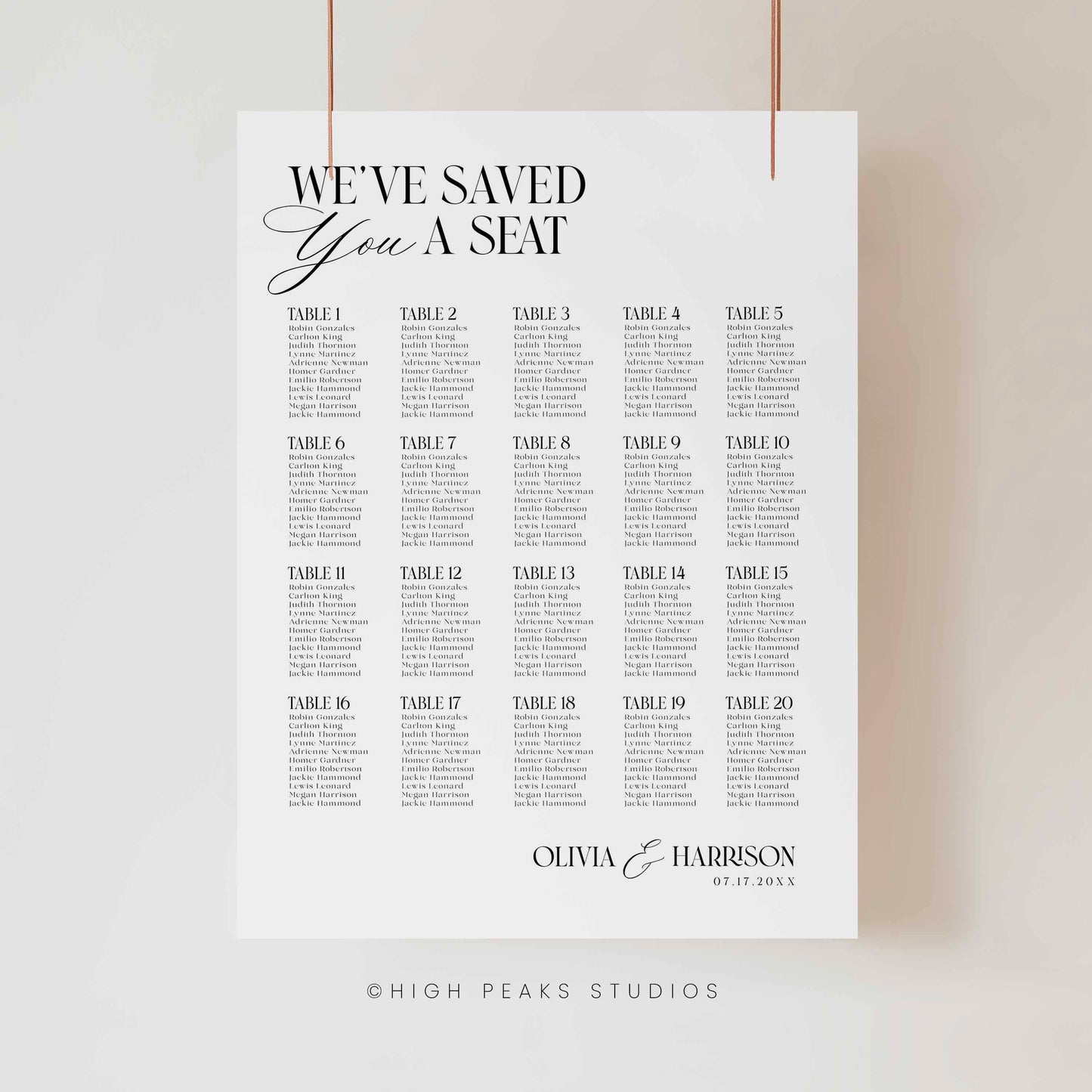 A vertical white wedding seating chart print hanging from two thin cords against a light neutral wall. The print features the text 'WE'VE SAVED YOU A SEAT' at the top, followed by a grid of table numbers from Table 1 to Table 30 with placeholder event text beneath each.